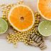 Citrus slices, small yellow supplement beads, and brown capsules on a wooden surface